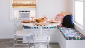 A dining area with a pink ceiling, a round table with clear chairs, and a bench with colorful cushions. - Tree Top Getaway- Sleeps 4 (Gulfport)