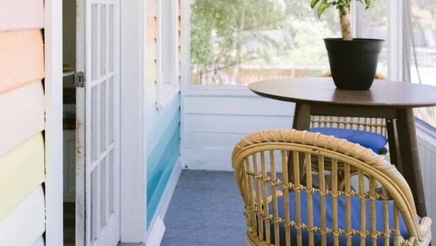 A covered porch with a wicker chair, a table with a potted plant, and a door leading to a room. - Tree Top Getaway- Sleeps 4 (Gulfport)