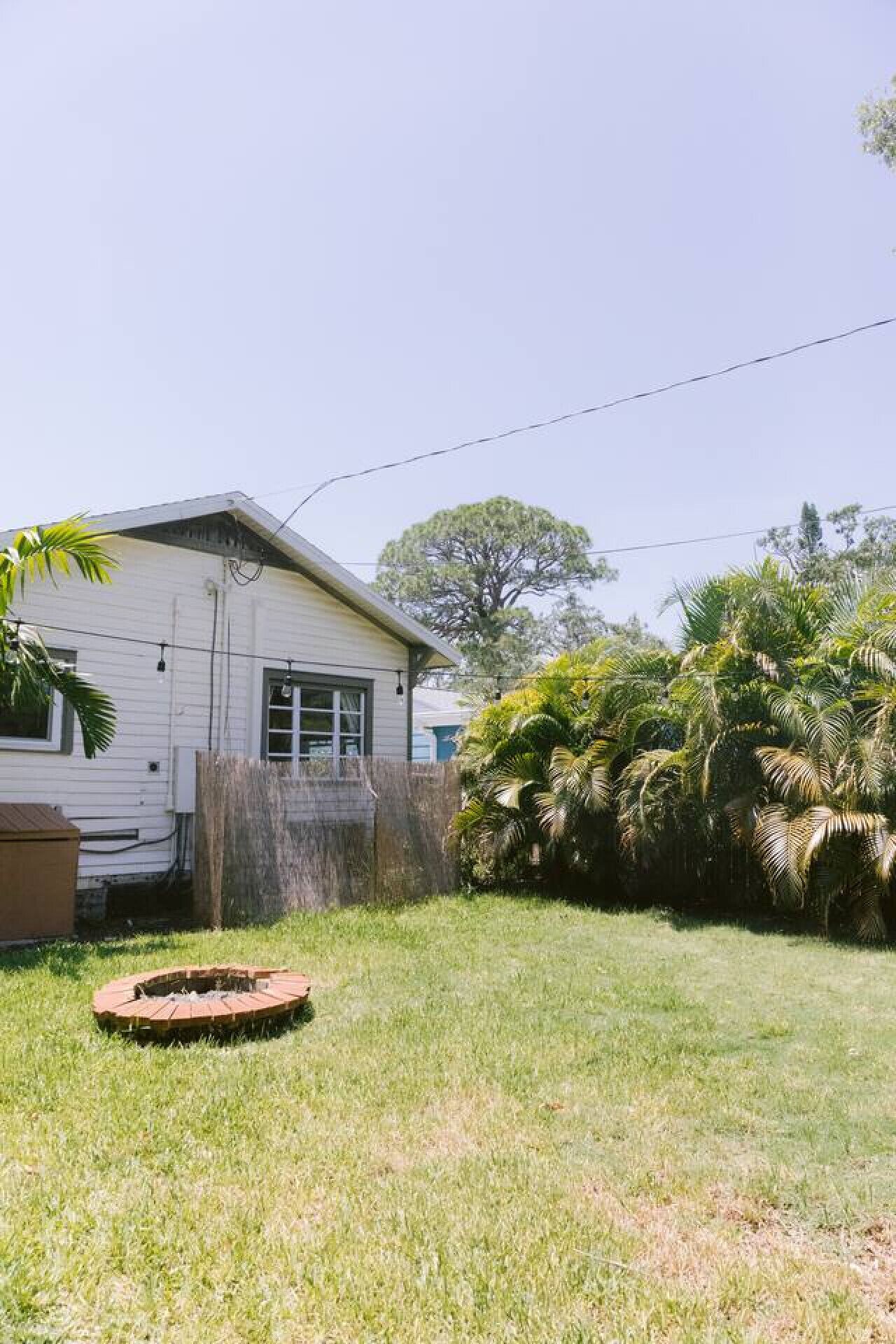 A single-story house with a fenced yard, a small circular fire pit, and lush greenery.