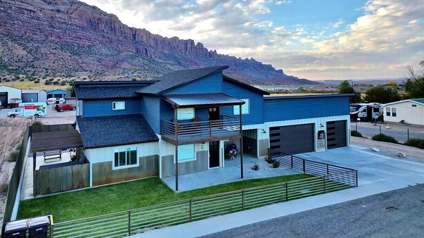 A modern two-story house with a balcony, garage, and a view of a mountainous landscape. - Amazing custom new home with modern amenities for a memorable and comfortable stay. (Moab)