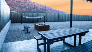 A patio with a wooden table and benches, a hammock, and a fire pit. - Amazing custom new home with modern amenities for a memorable and comfortable stay. (Moab)