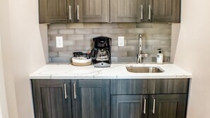 A compact kitchen with dark wood cabinets, a marble countertop, a coffee maker, and a sink. - Amazing custom new home with modern amenities for a memorable and comfortable stay. (Moab)