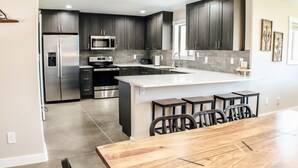 A modern kitchen with dark cabinets, stainless steel appliances, and a central island with bar stools. - Amazing custom new home with modern amenities for a memorable and comfortable stay. (Moab)