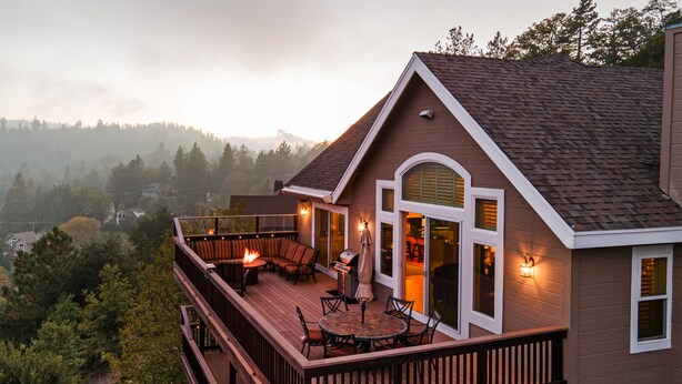 Une maison à deux étages dotée d’une terrasse, d’un espace salon extérieur et d’une cheminée.
