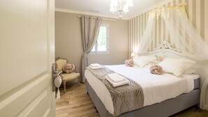 Een slaapkamer met een bed, een stoel, een raam met gordijnen en een kroonluchter.