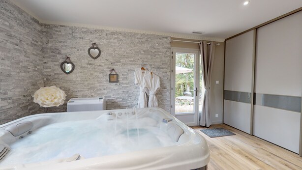 Een moderne badkamer met een ruime badkuip, een douche en een glazen deur naar een buitenruimte.