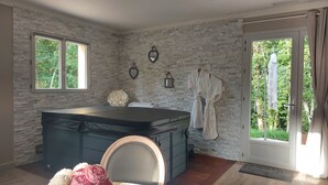 Een wellnessruimte met een stenen muur, een massagetafel, een grote spiegel en een badjas hangend aan de muur.