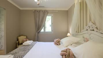 Een slaapkamer met een bed, gordijnen, een stoel en een kroonluchter.