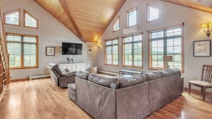 A spacious living room with a large sectional sofa, wooden flooring, and multiple windows providing natural light.