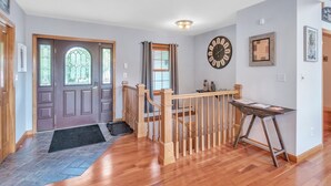 A hallway with a wooden railing, a clock on the wall, and a desk with a chair.