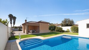 Une piscine à l’eau d’un bleu limpide, une terrasse avec des meubles d’extérieur et un petit bâtiment doté d’un toit en tuiles.