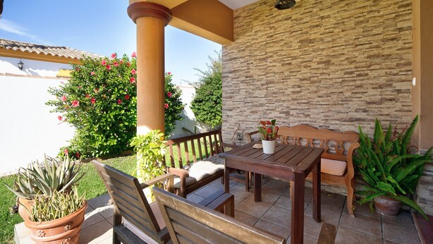 Une terrasse extérieure avec une table et des bancs en bois, entourée de plantes en pot et d’un mur de pierre.