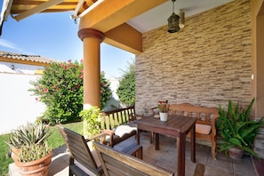 Une terrasse extérieure avec une table et des bancs en bois, entourée de plantes en pot et d’un mur de pierre.