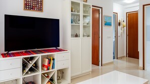 A living room with a flat-screen TV, white cabinets, and a tiled floor.