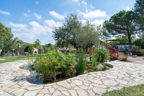 Uma trilha de pedra que leva a um lago com plantas, uma ponte vermelha e árvores em um parque.