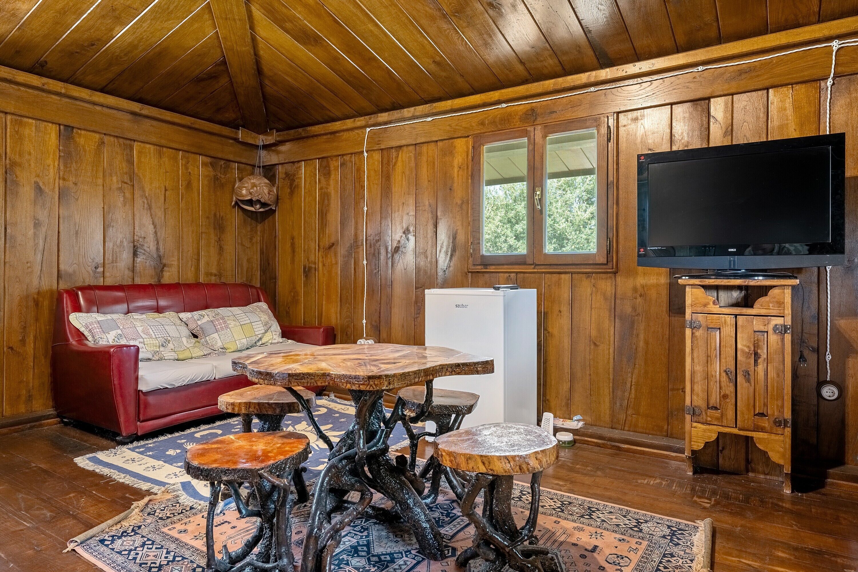 L’intérieur d’un chalet en bois, avec un canapé rouge, un téléviseur et un réfrigérateur.