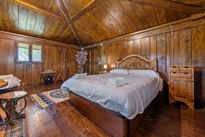 Quarto de madeira com uma cama grande, uma mesinha e um armário.