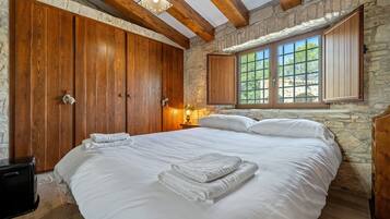 A bedroom with a large bed, wooden wardrobe, stone walls, and a window with shutters.