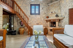 A stone-walled room with a wooden staircase, a white sofa, a wooden coffee table with a vase of flowers, and a fireplace. - Chalet "Casa de Pedra" with Mountain View, Shared Pool & Wi-Fi (Querol)