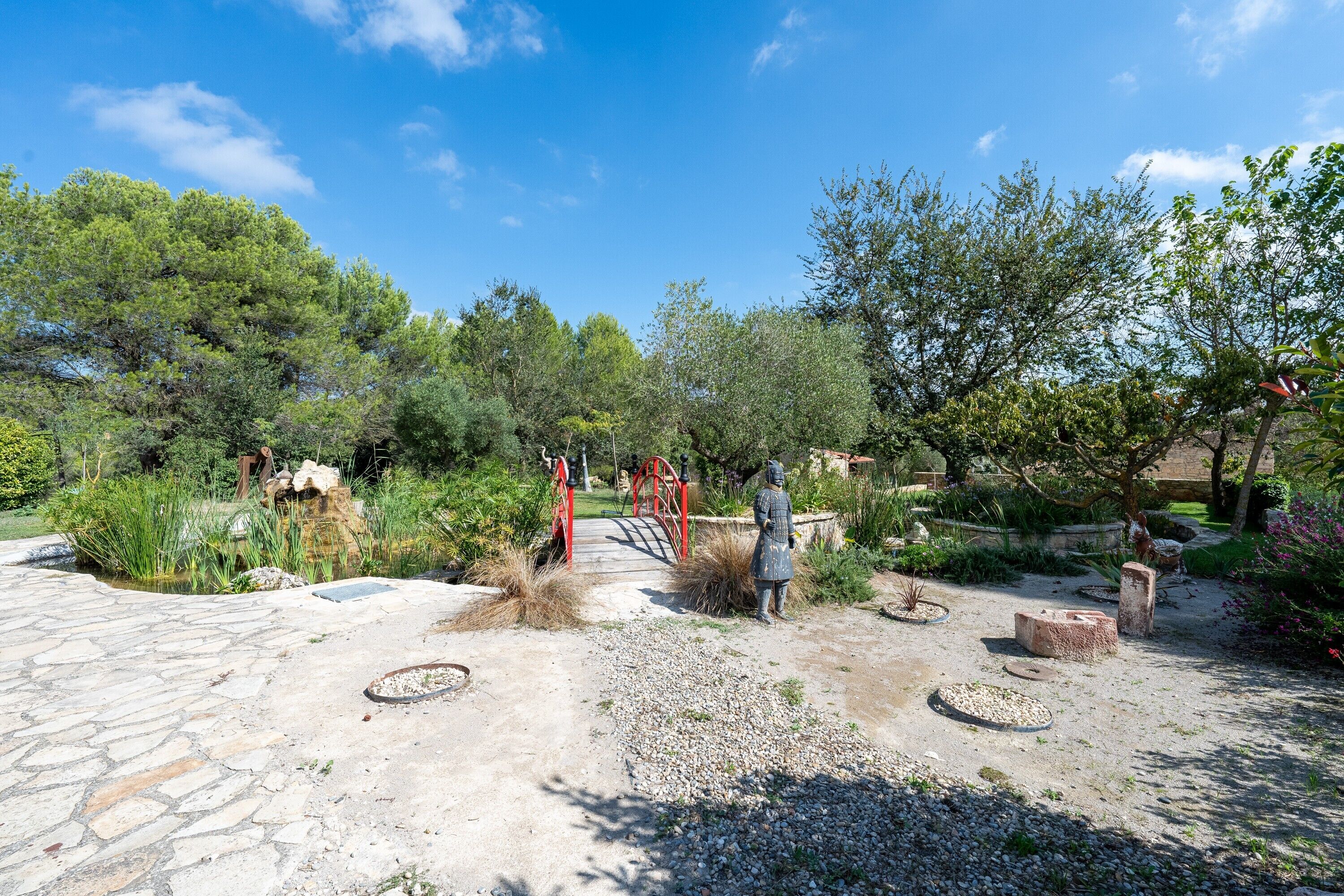 Un jardin avec un sentier en pierre, un pont rouge et une statue.