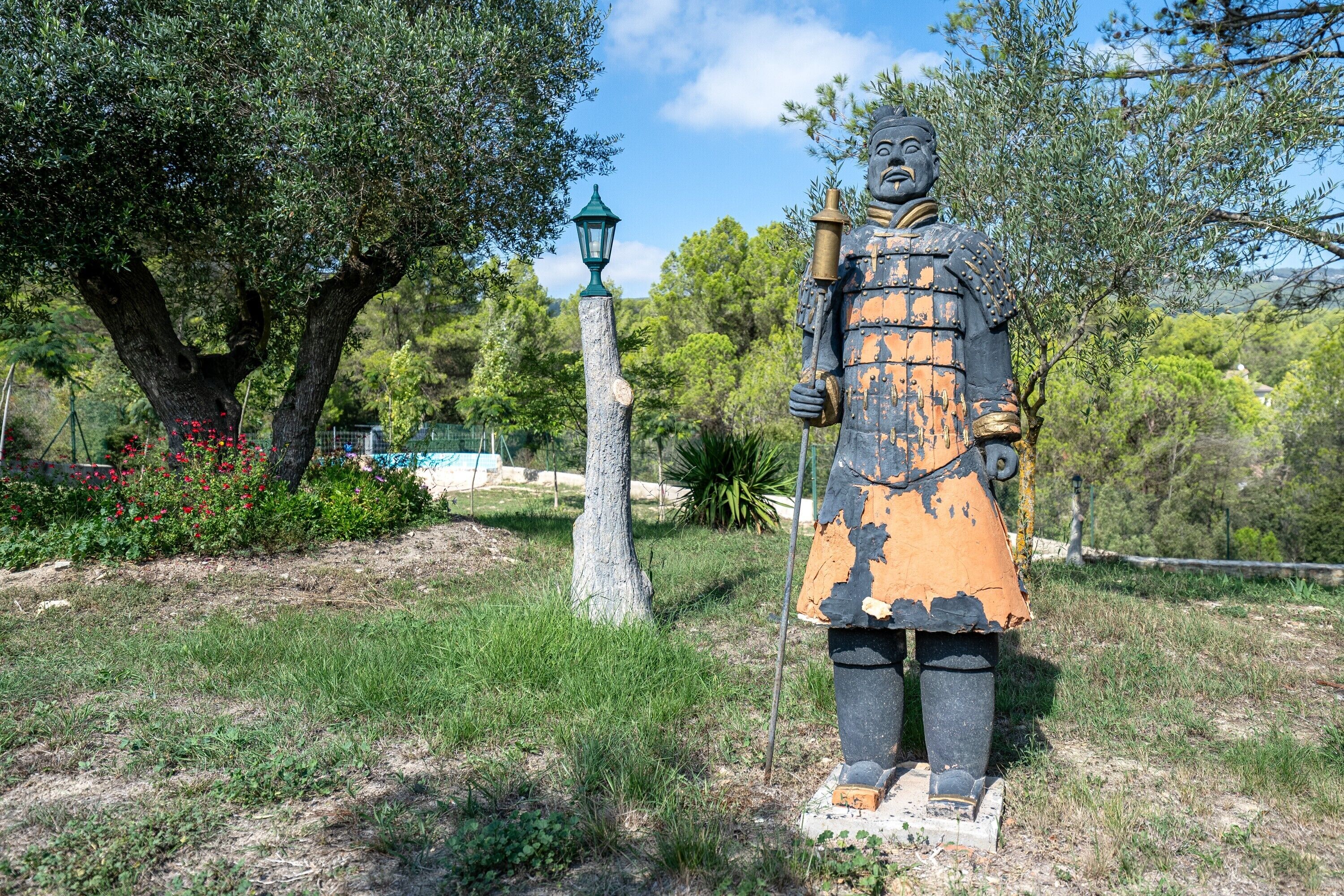 Eine Statue in einem Park mit Bäumen und einer Lampe.