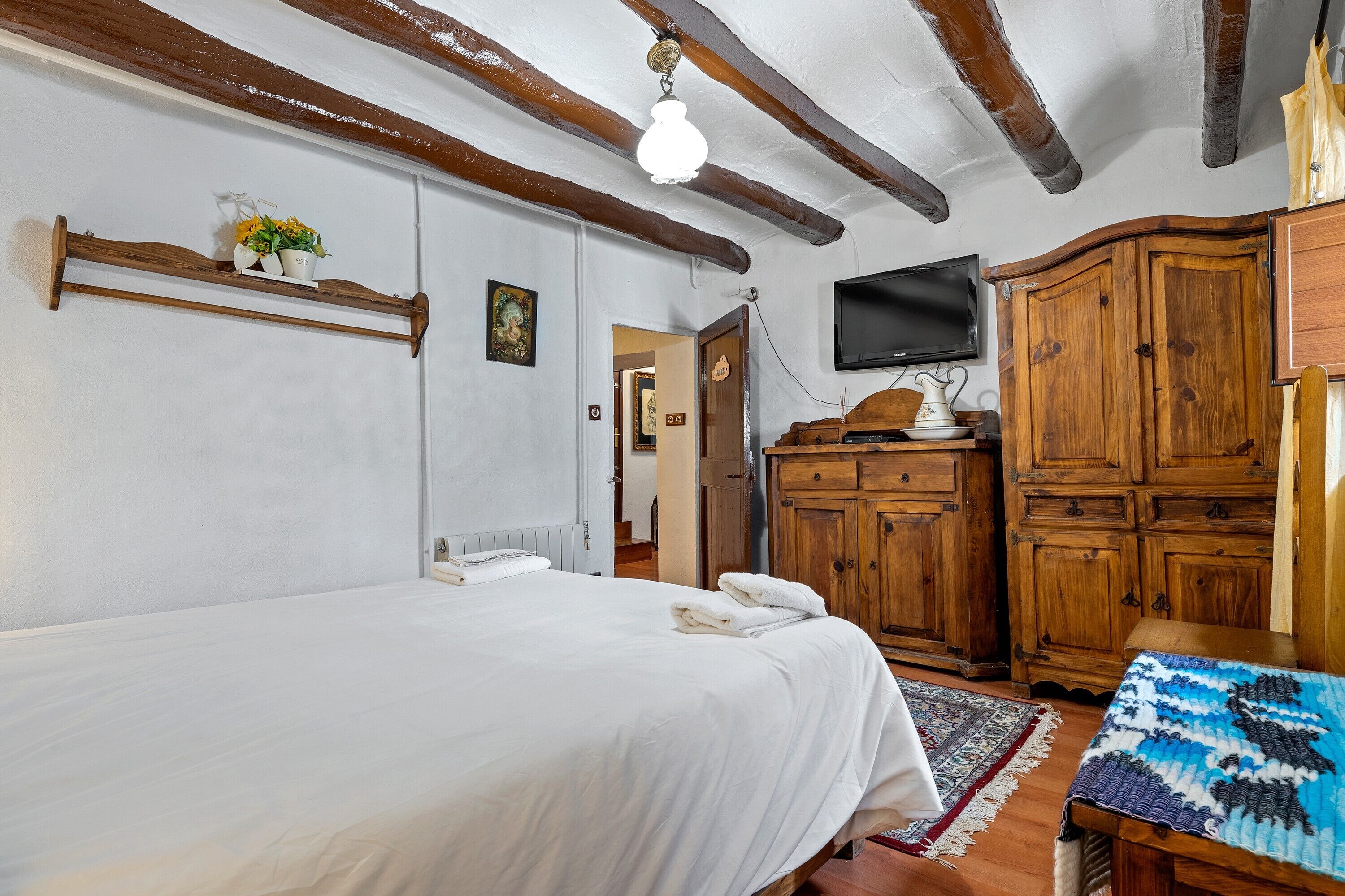 A bedroom with a bed, wooden wardrobe, TV, and a shelf with flowers.