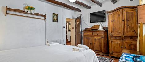 A bedroom with a bed, wooden wardrobe, TV, and a shelf with flowers.