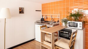 A compact kitchen with a wooden table, two chairs, a microwave, a toaster, and a small refrigerator.