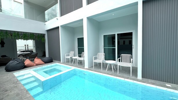 Un'area piscina moderna al coperto, con vasca di colore blu intenso, sedie bianche e un angolo relax con cuscini.