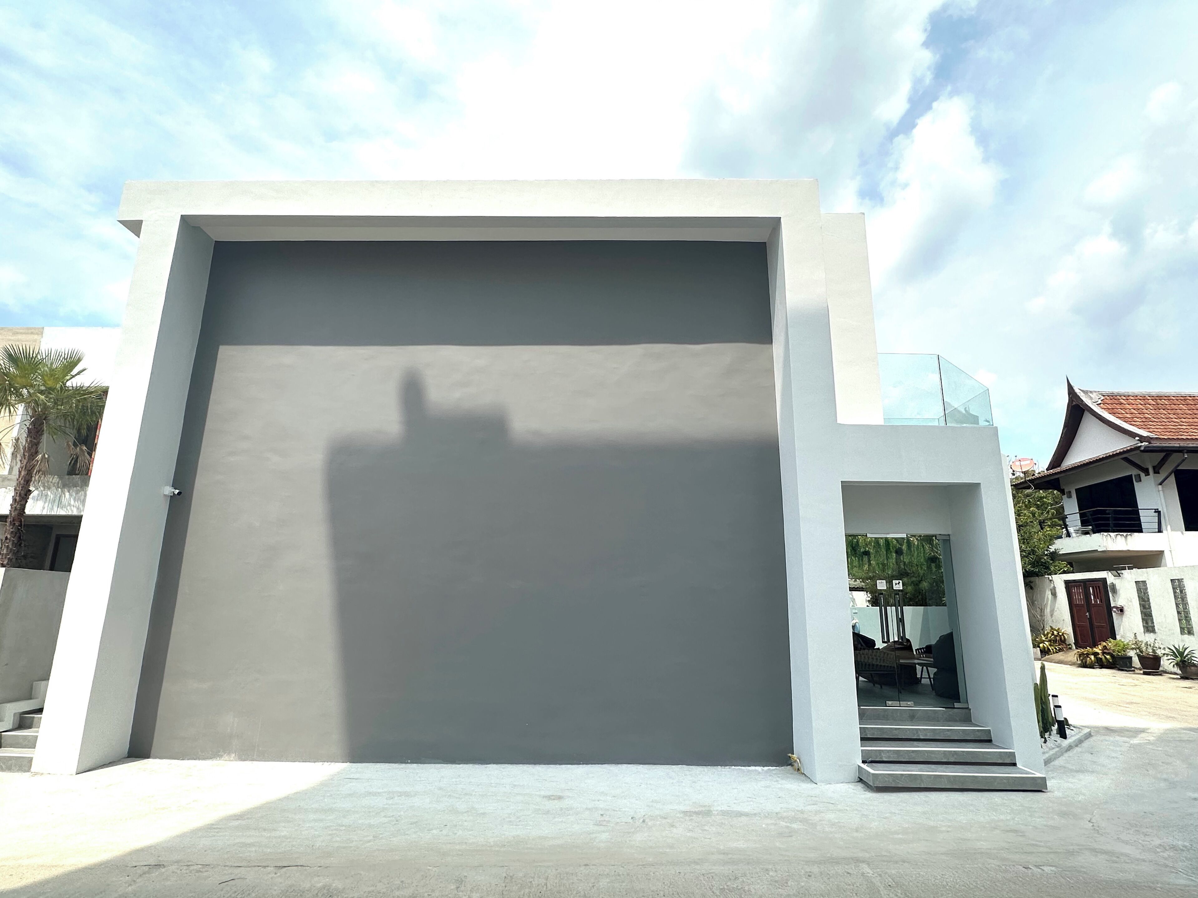 Un bâtiment moderne doté d’une grande porte de garage, d’un escalier menant à une entrée abritée et, en arrière-plan, d’un ciel dégagé.