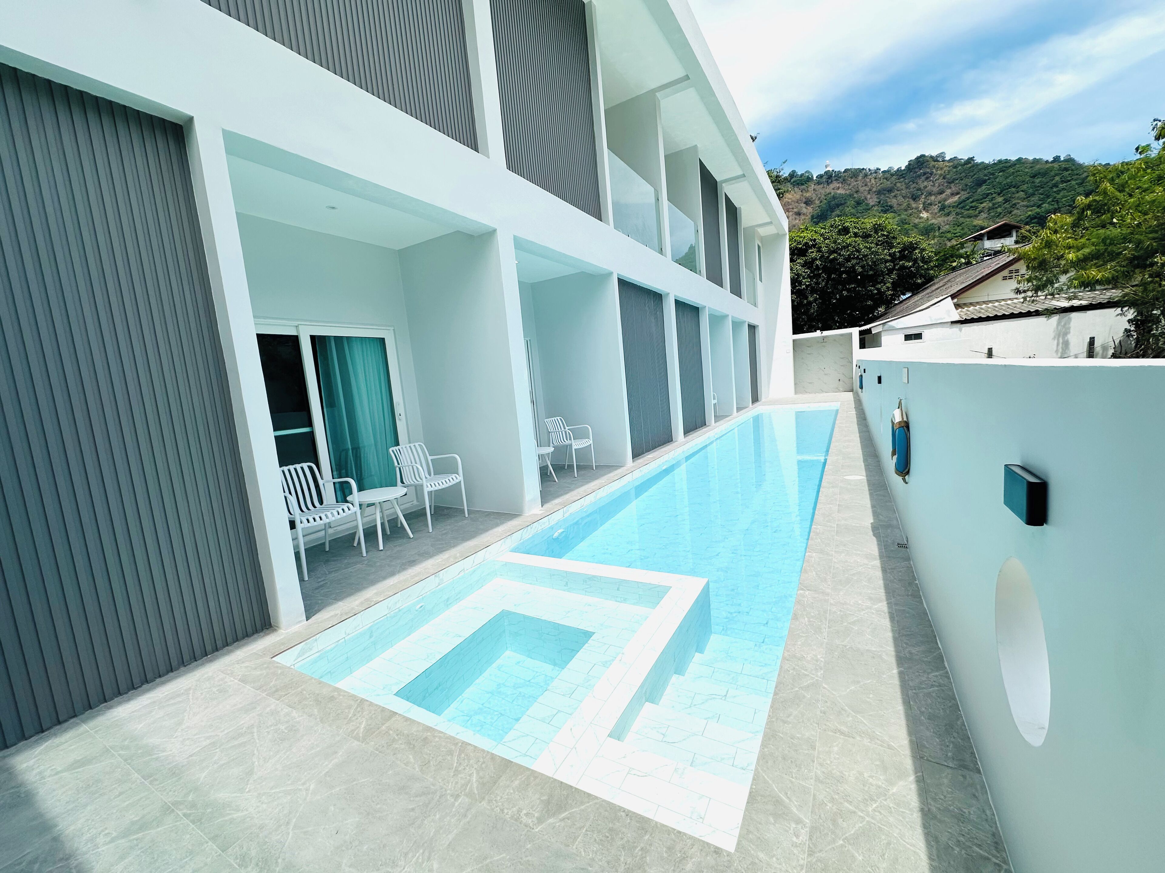 Un edificio moderno con piscina, mobiliario exterior y vistas a una colina.