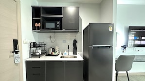 Una cucina moderna con frigorifero nero, forno a microonde e pensili neri. Si nota un lavello, un bollitore e una sedia.
