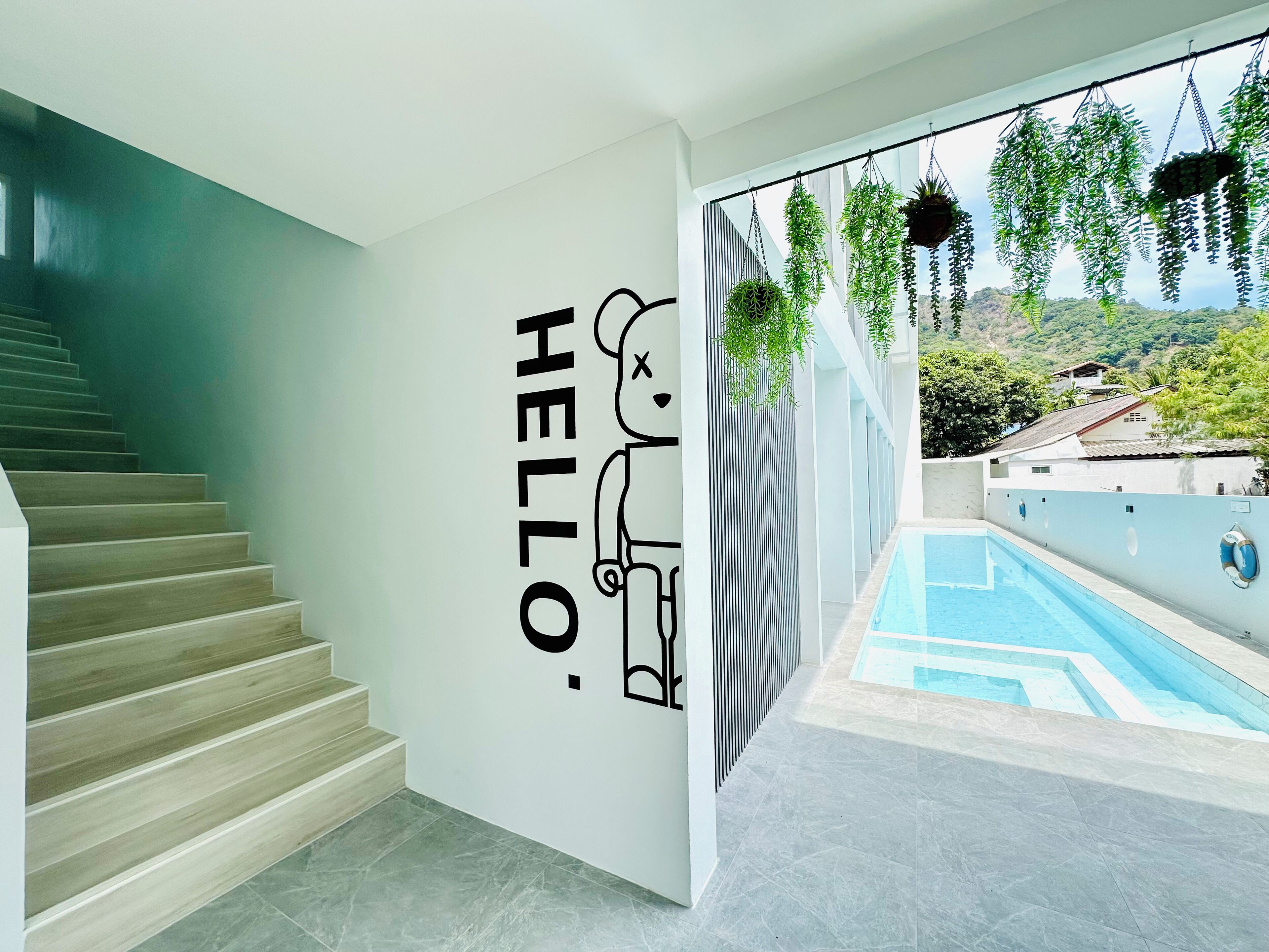 A modern interior with a staircase, a wall with a 'HELLO' sign, and a pool area with hanging plants.