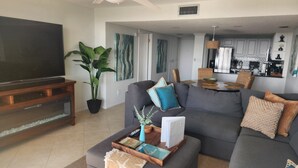 A living room with a large grey sofa, a coffee table with books and a vase, a TV, and a potted plant. - Anchorage 808 (Siesta Key)