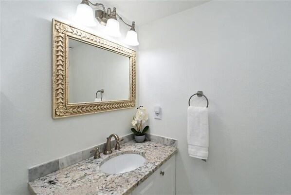 A bathroom with a marble sink, a gold-framed mirror, and a towel rack.