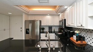 A modern kitchen with white cabinetry, a black countertop, stainless steel appliances, and a built-in microwave. - Anchorage 808 (Siesta Key)
