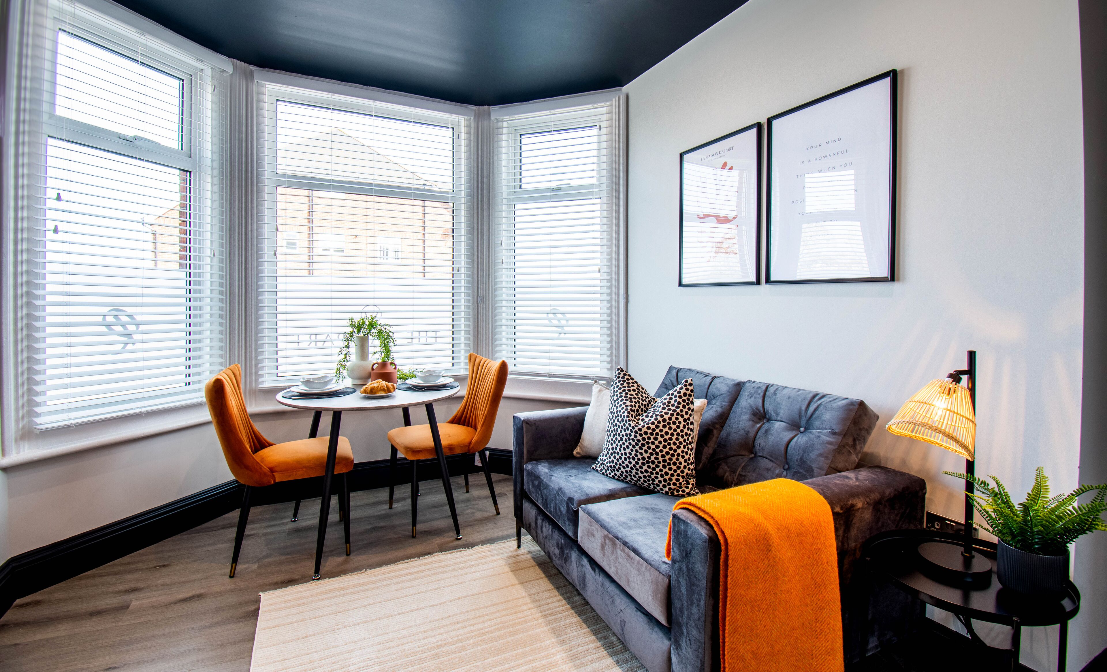 A modern living room with a gray sofa, orange chairs, a round table, and a potted plant.