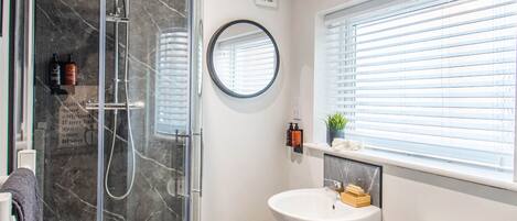 A bathroom with a glass-enclosed shower, a pedestal sink, a toilet, and a window with blinds.