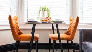 A dining area with two orange chairs, a small table, and a window with blinds.