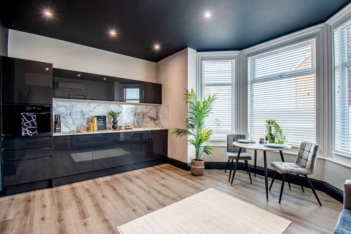 A modern kitchen with black cabinets, a marble countertop, and a dining area with a table and chairs.