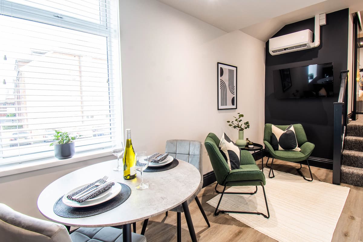 A modern living room with a dining area, a staircase, and a TV mounted on the wall.
