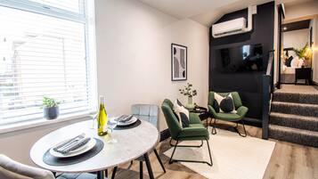 A modern living room with a dining area, a staircase, and a TV mounted on the wall.
