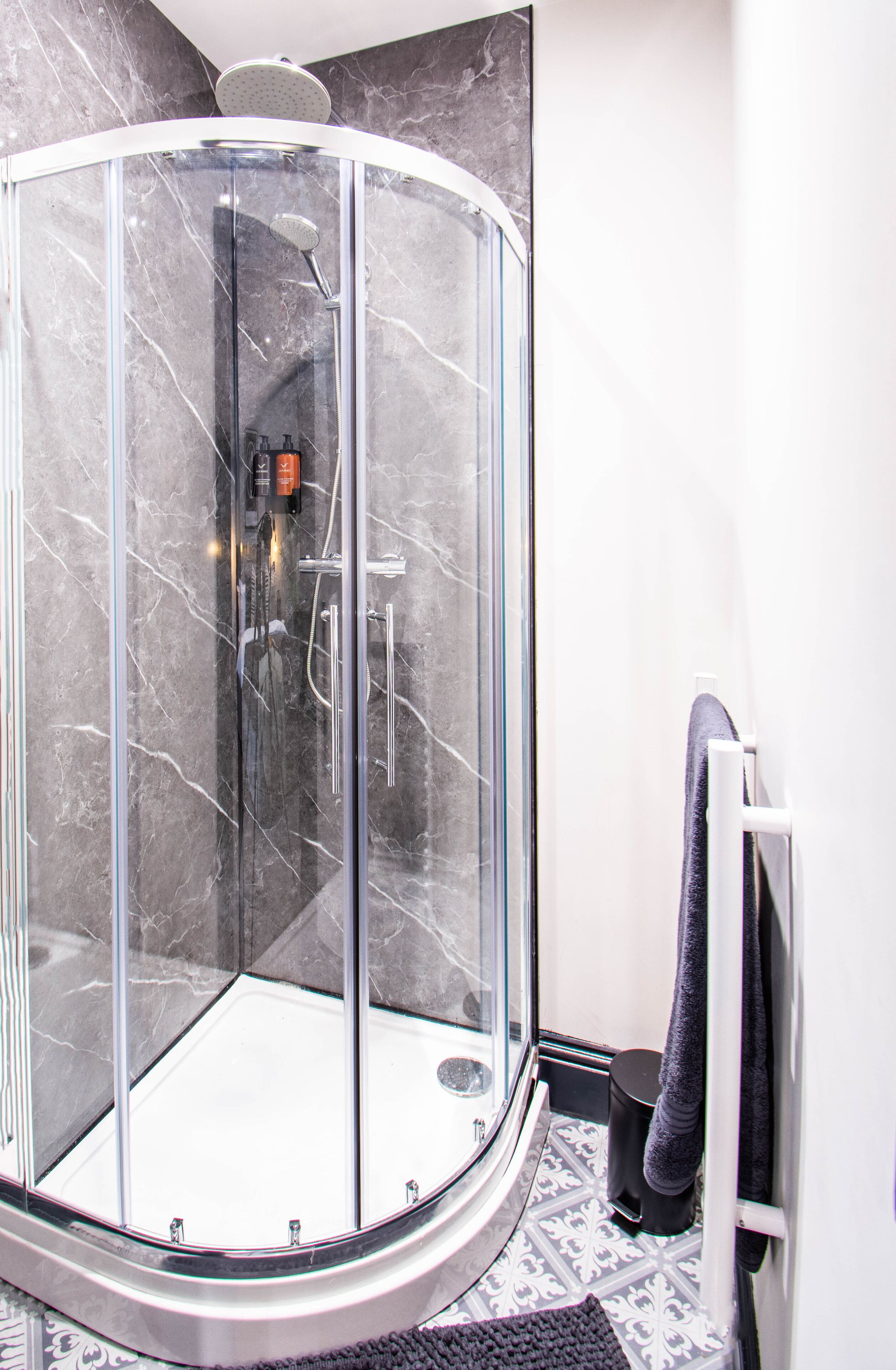 Une douche fermée par des parois en verre, dotée d’un design incurvé, d’un pommeau de douche à main et d’un panneau de commande.