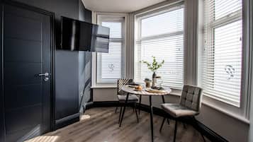 A modern kitchen with a dark cabinetry, a flat-screen TV mounted above the counter, and a dining area with a round table and two chairs.