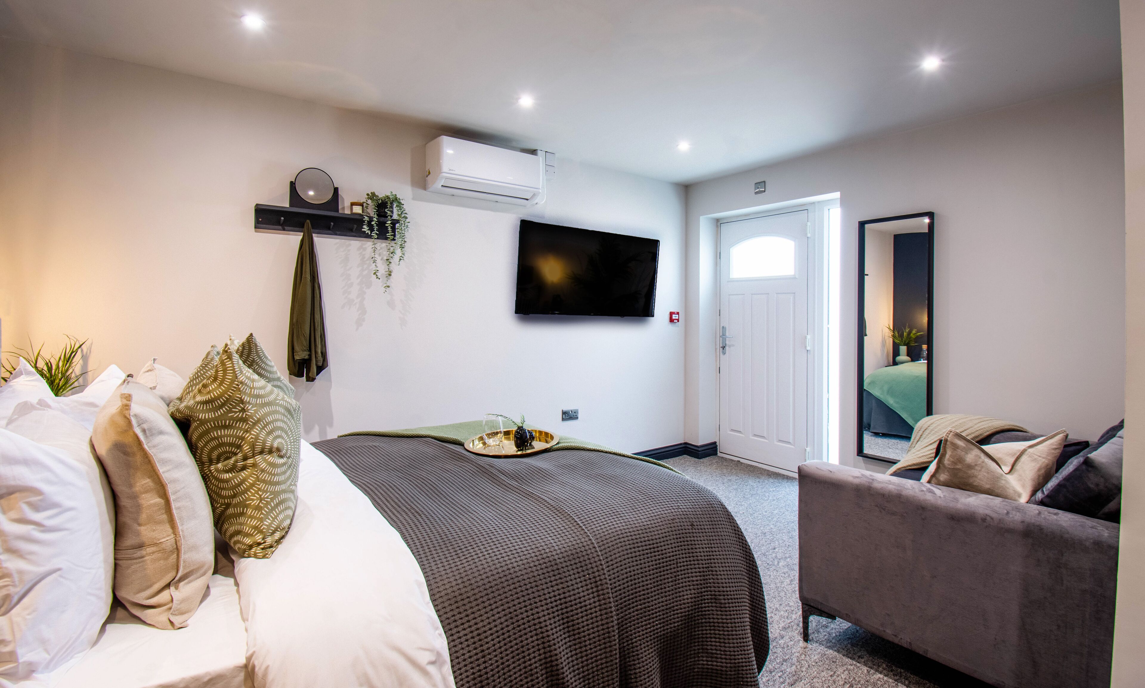 Un dormitorio moderno con cama, sofá, televisor y una puerta.