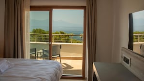 A hotel room with a bed, a desk, and a balcony with a view of the sea and mountains. - Ömer Prime Holiday Resort (Kusadasi)