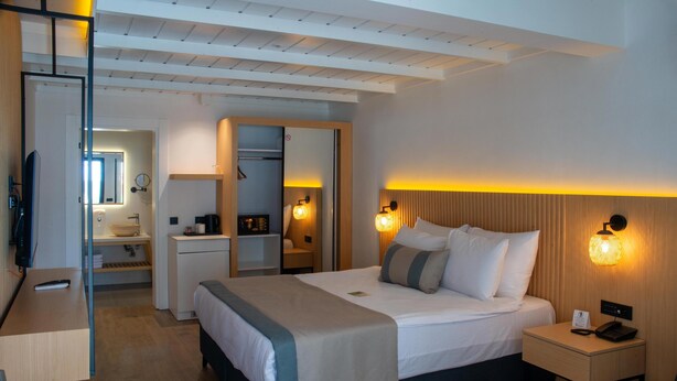 A hotel room with a bed, bedside table, and a desk with a chair. - Ömer Prime Holiday Resort (Kusadasi)