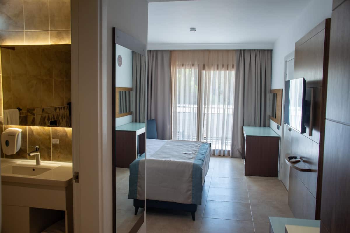 A hotel room with a bed, a desk, a TV, a bathroom with a sink, and a mirror.