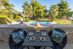 A patio with a table set for two, a pool, and a children's play area in the background. - Enjoy your vacation at a luxurious stone villa with garden & swimming pool! (Agioi Theodoroi)