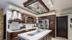 A modern kitchen with wooden cabinets, a stainless steel refrigerator, and a large island with a marble countertop.